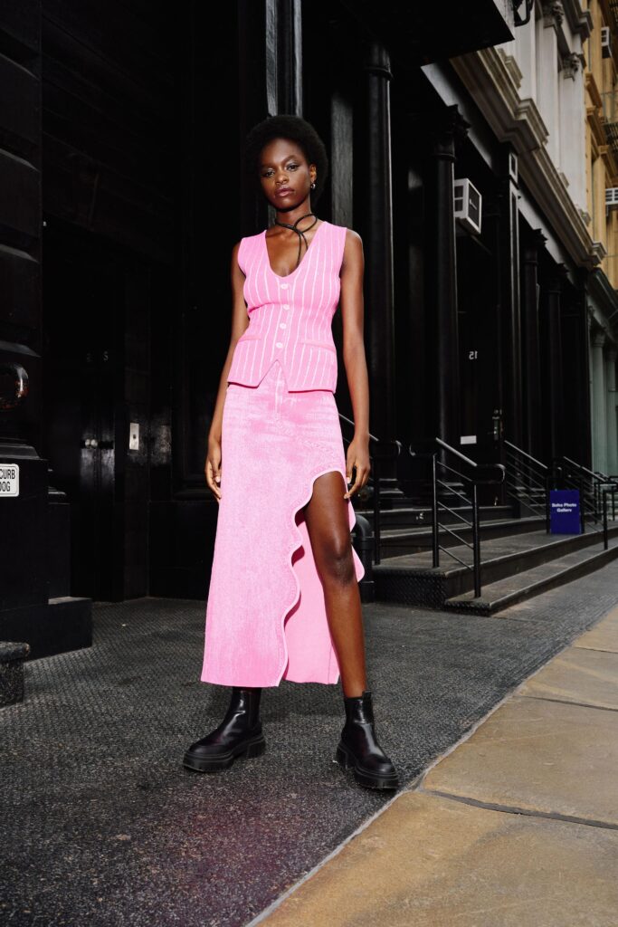A fitted pink sleeveless vest paired with a high-waisted asymmetric skirt featuring a slit.