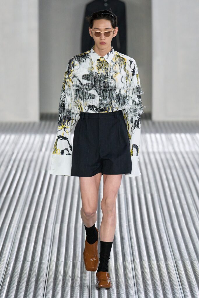 A fitted white printed shirt with long sleeves and collared design paired with black shorts.