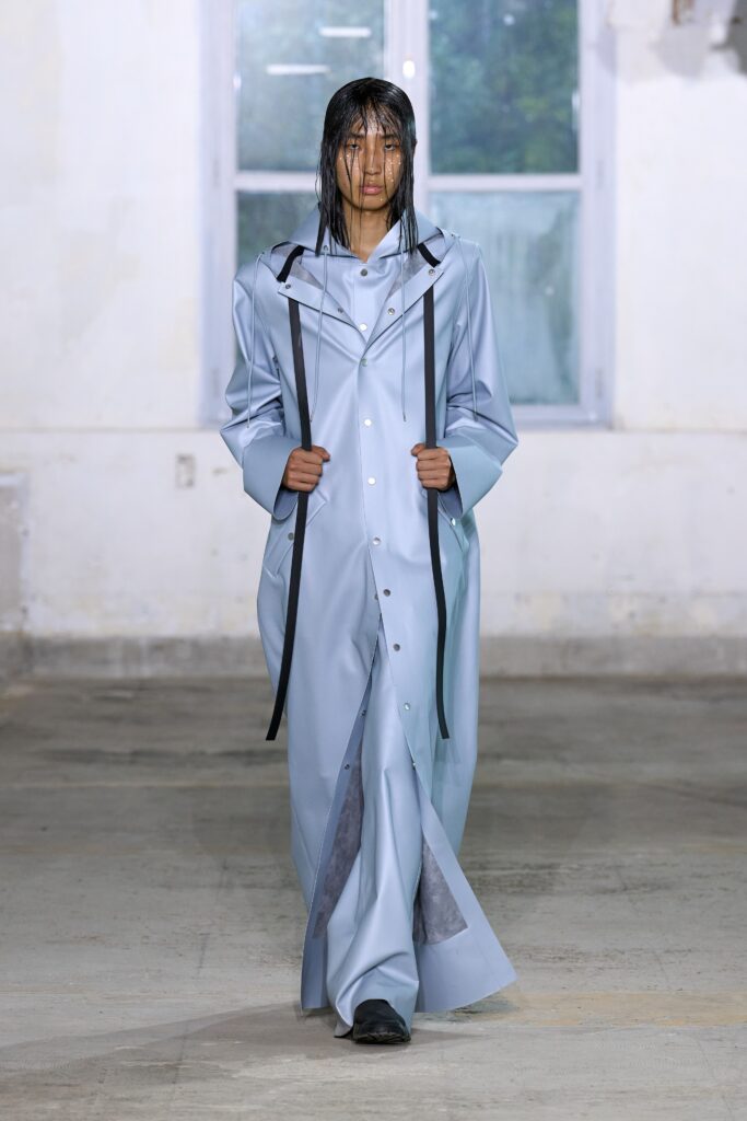 A relaxed blue cotton coat dress with long sleeves and a collared neckline, featuring buttoned and layered details.