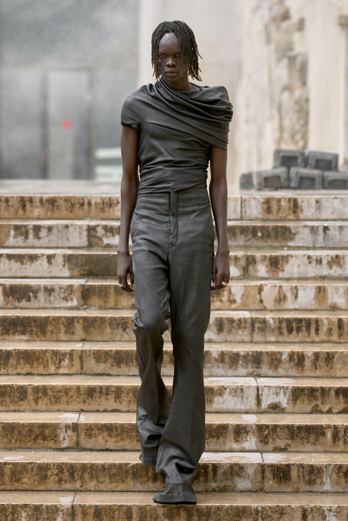 A fitted gray sleeveless top with an asymmetric design paired with high-waisted pants.