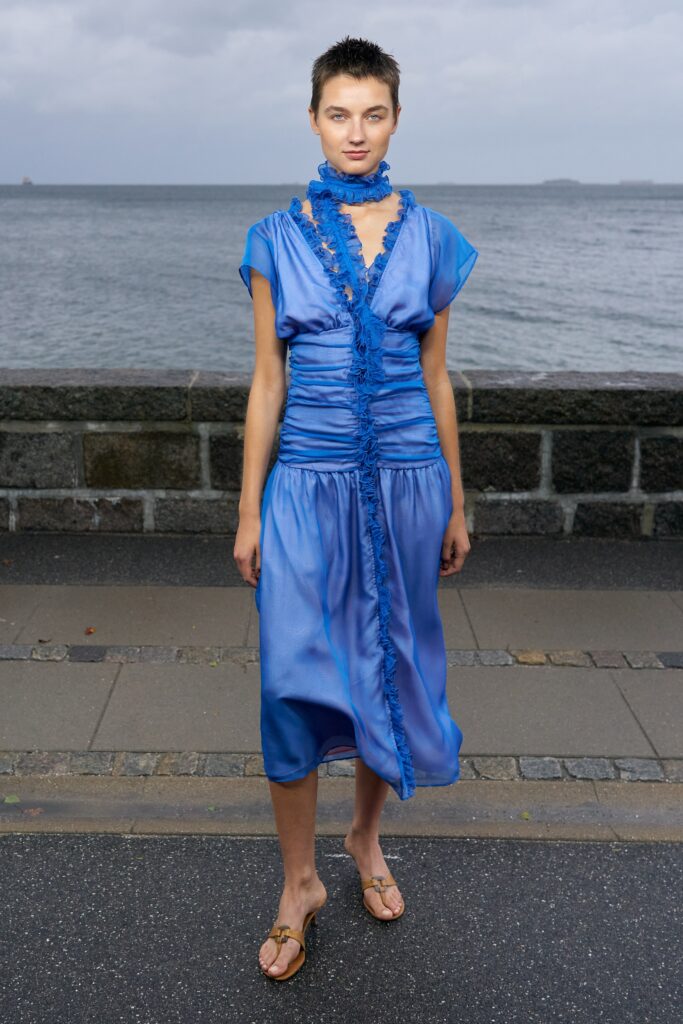 A fitted blue silk dress with short sleeves and a V-neckline featuring draped detailing.