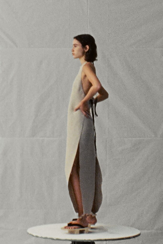 A fitted beige silk sleeveless dress featuring a V-neckline and a high slit.