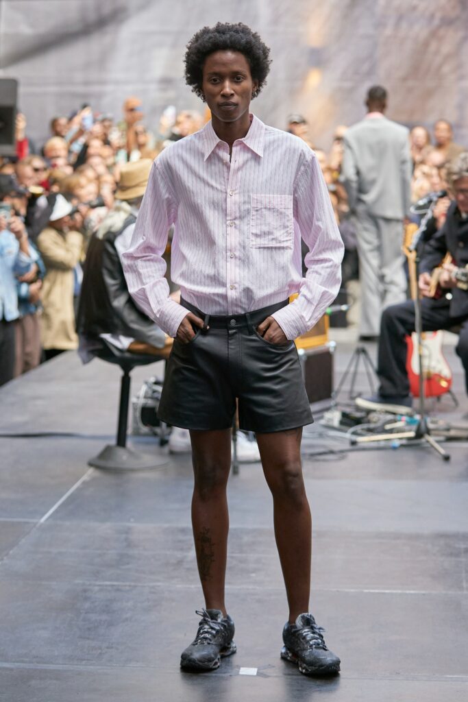 A fitted pink long-sleeve collared shirt paired with black leather shorts.