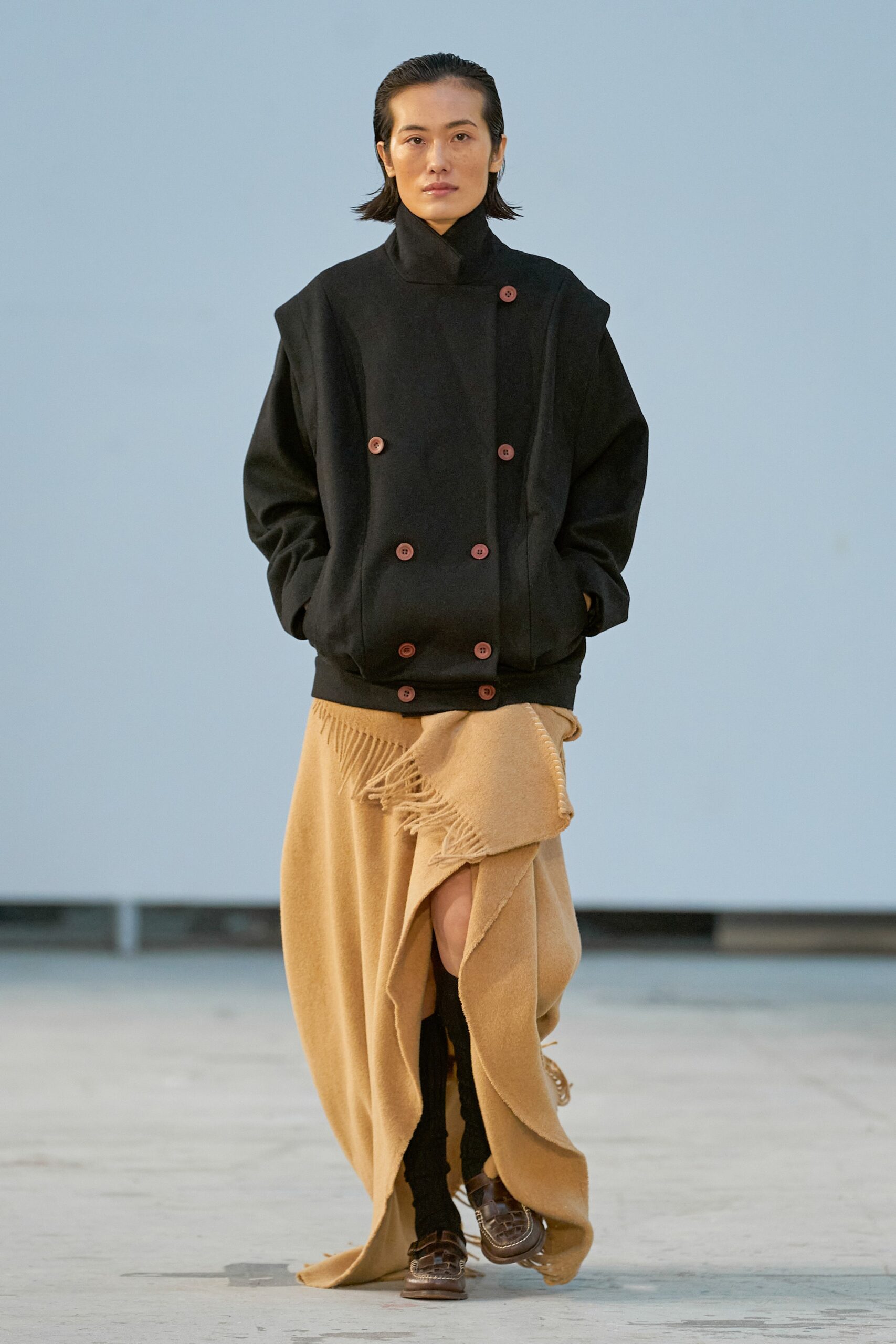 A relaxed black wool coat with long sleeves and a collared design, paired with an asymmetric beige skirt.