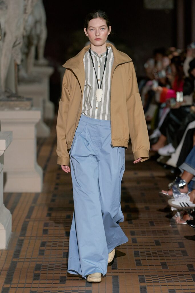 A relaxed-fit beige jacket with a collared neckline paired with wide-leg blue pants.