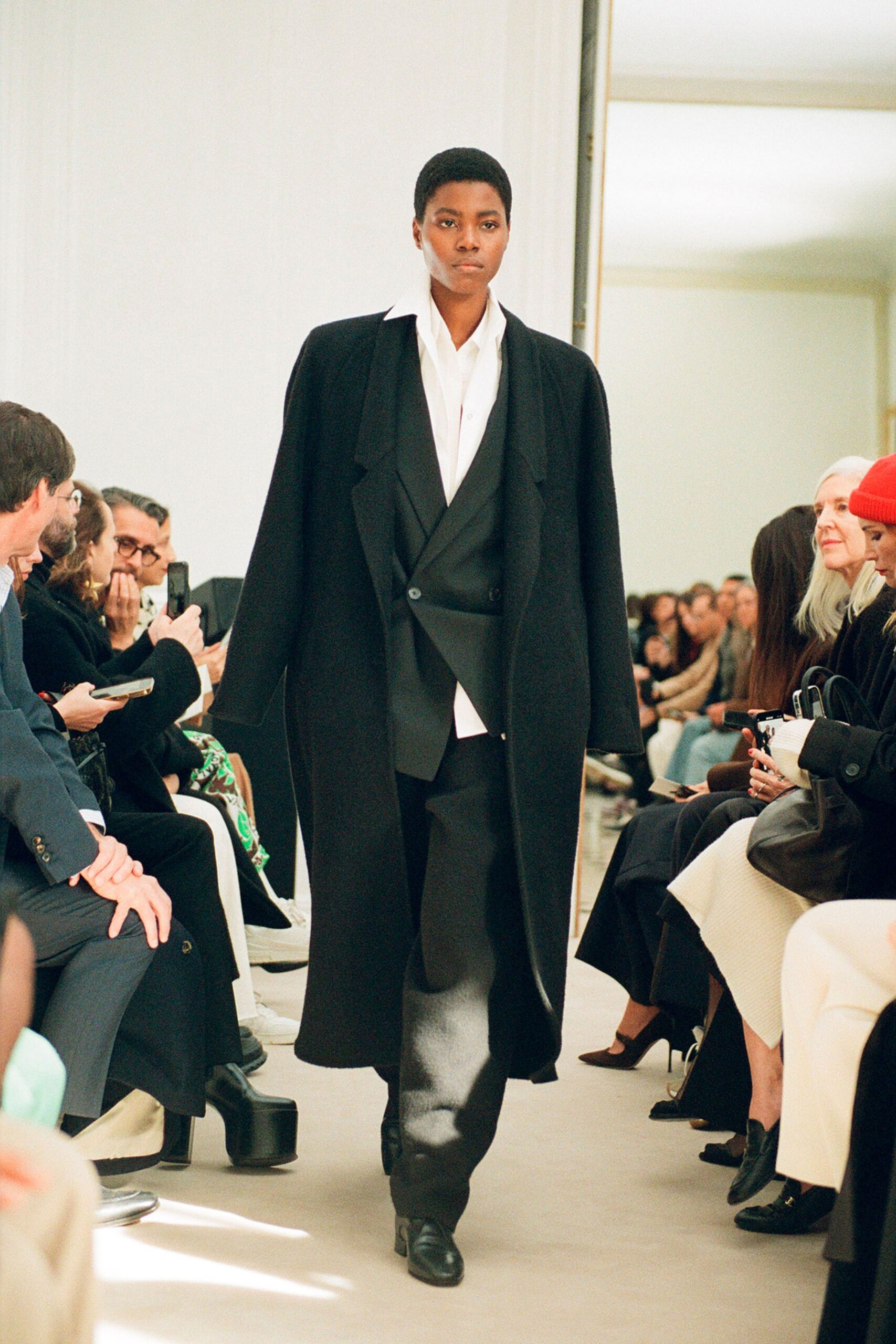 A relaxed black wool coat layered over a collared suit, featuring long sleeves.