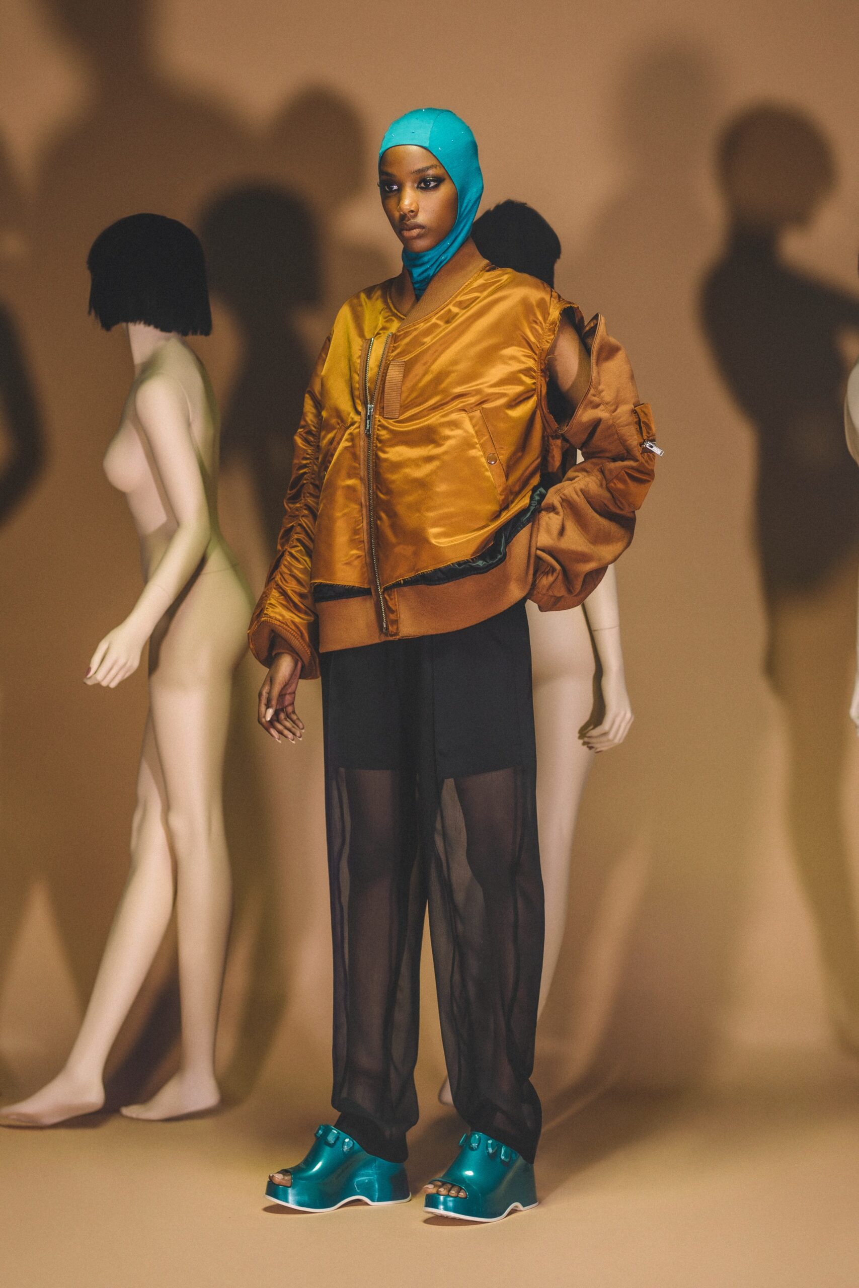 A relaxed brown jacket paired with black sheer pants, featuring a collared design and layered details.