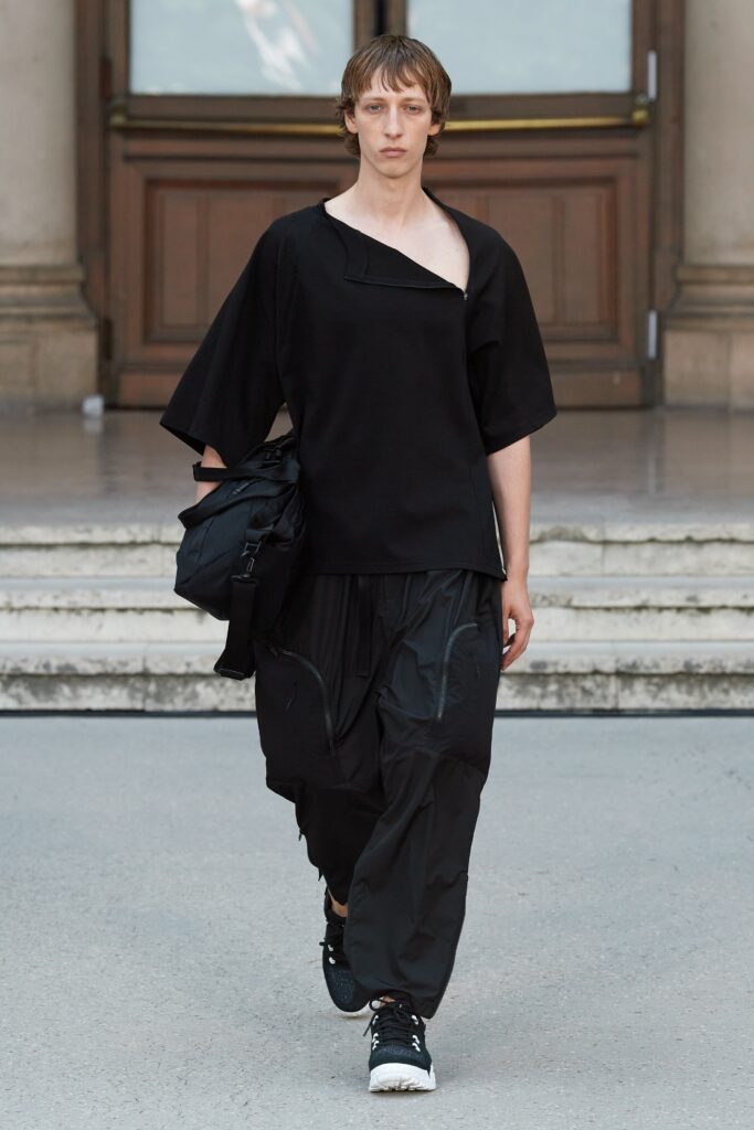 A relaxed black top with short sleeves and asymmetric design paired with black pants.
