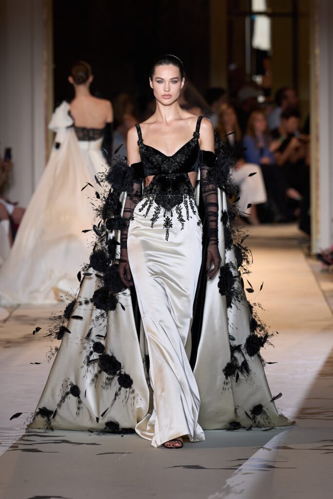A fitted black and white gown with a V-neckline, layered design, and intricate embroidery.