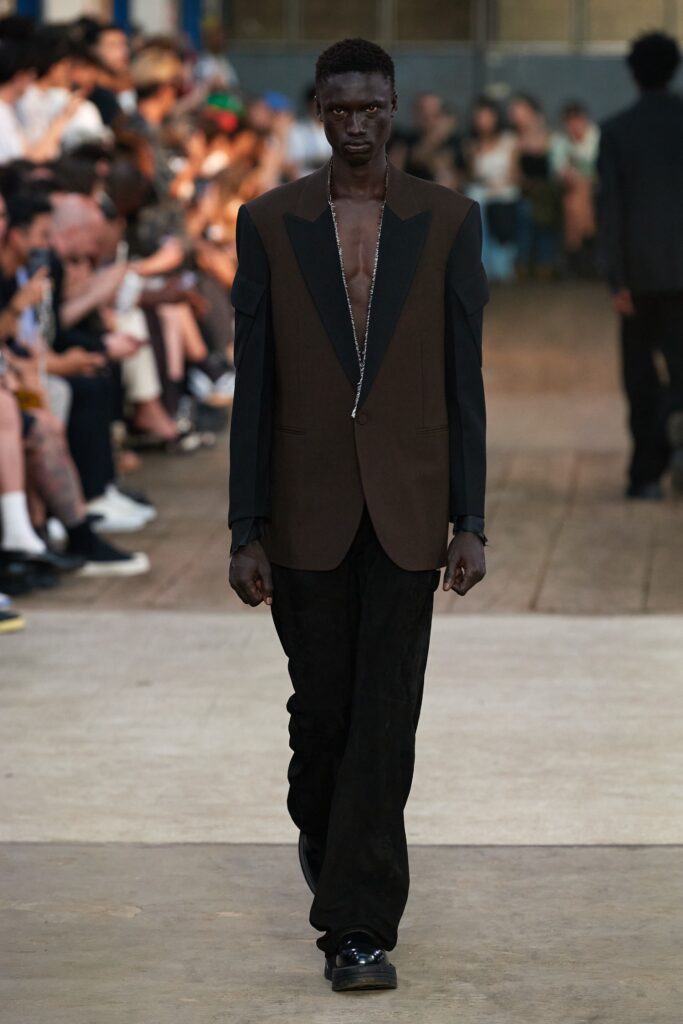 A fitted brown blazer paired with black pants featuring an asymmetric design.