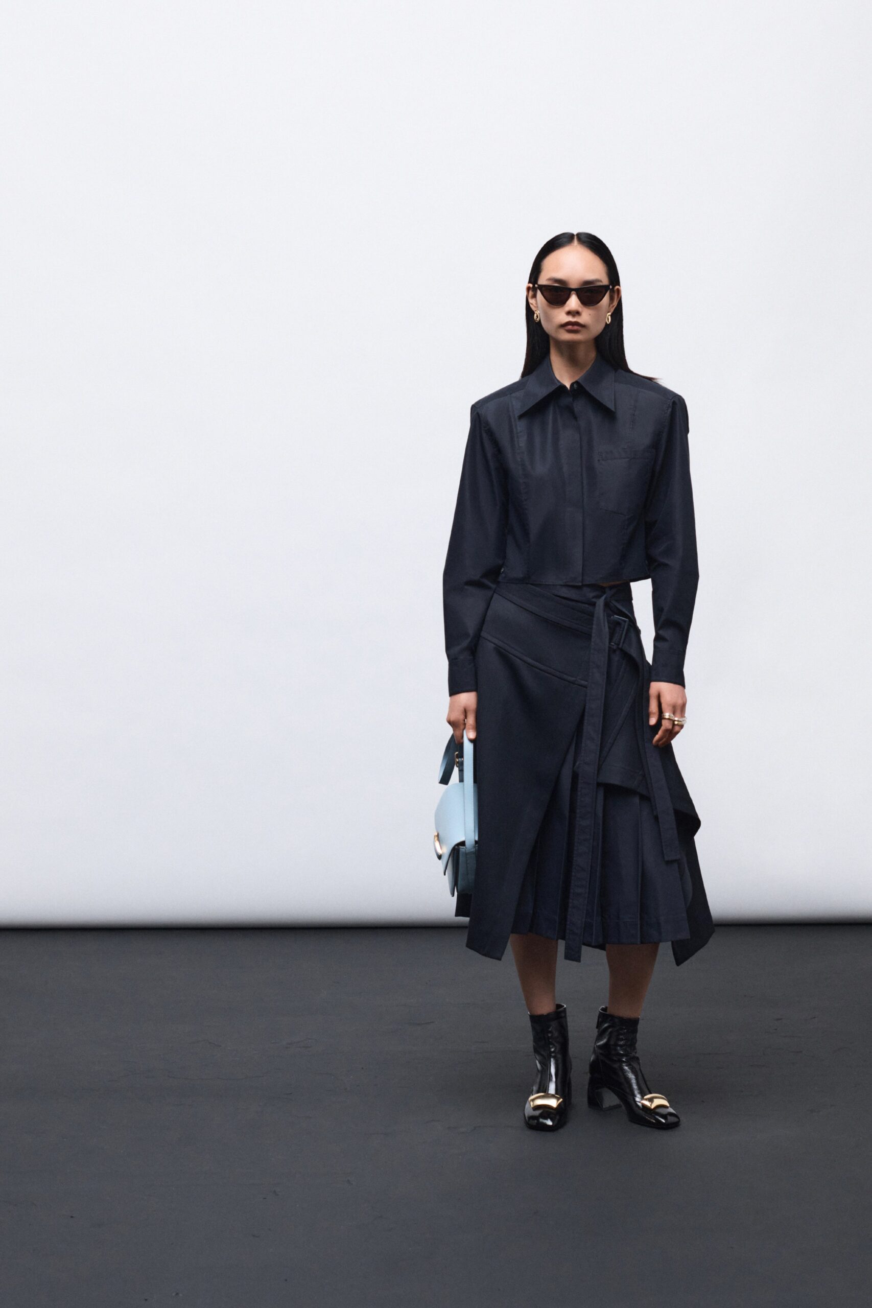 A fitted black long-sleeve dress with a collared neckline and asymmetric, belted design.