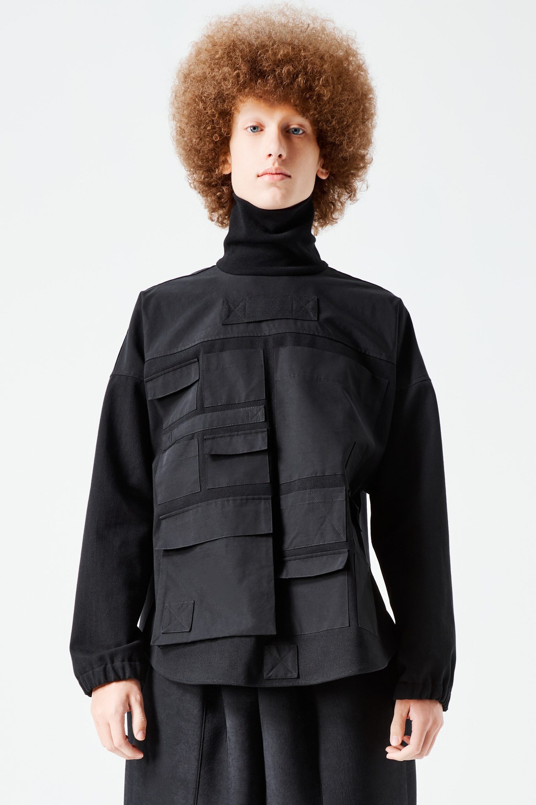 This relaxed top features a turtleneck design that adds a layer of sophistication. The asymmetric detailing and patchwork pockets create a visually intriguing silhouette, blending functionality with contemporary style.
