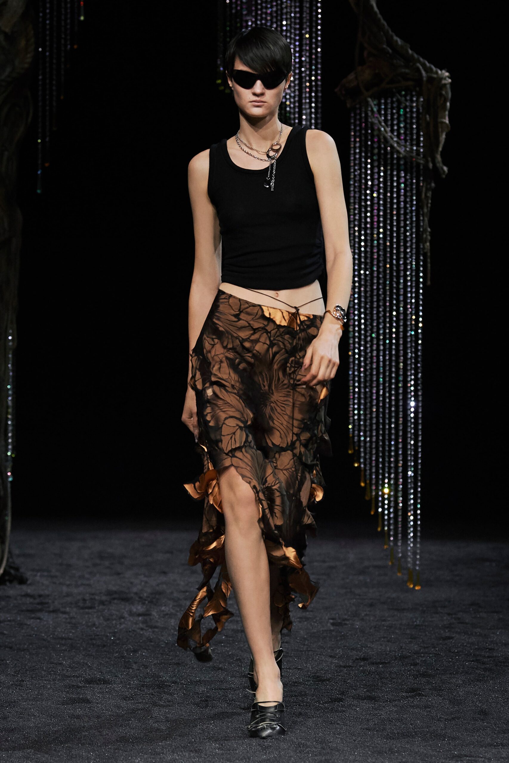 A fitted black sleeveless top paired with a high-waisted, asymmetric layered skirt in brown.