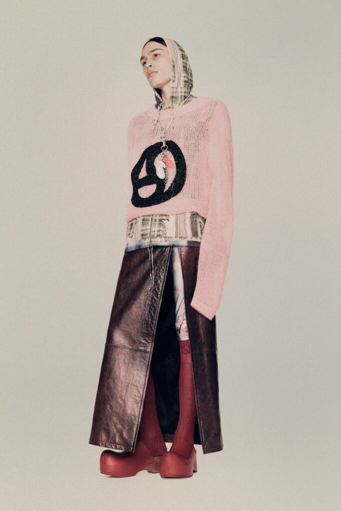 A relaxed pink knit sweater with long sleeves layered over a brown leather skirt.