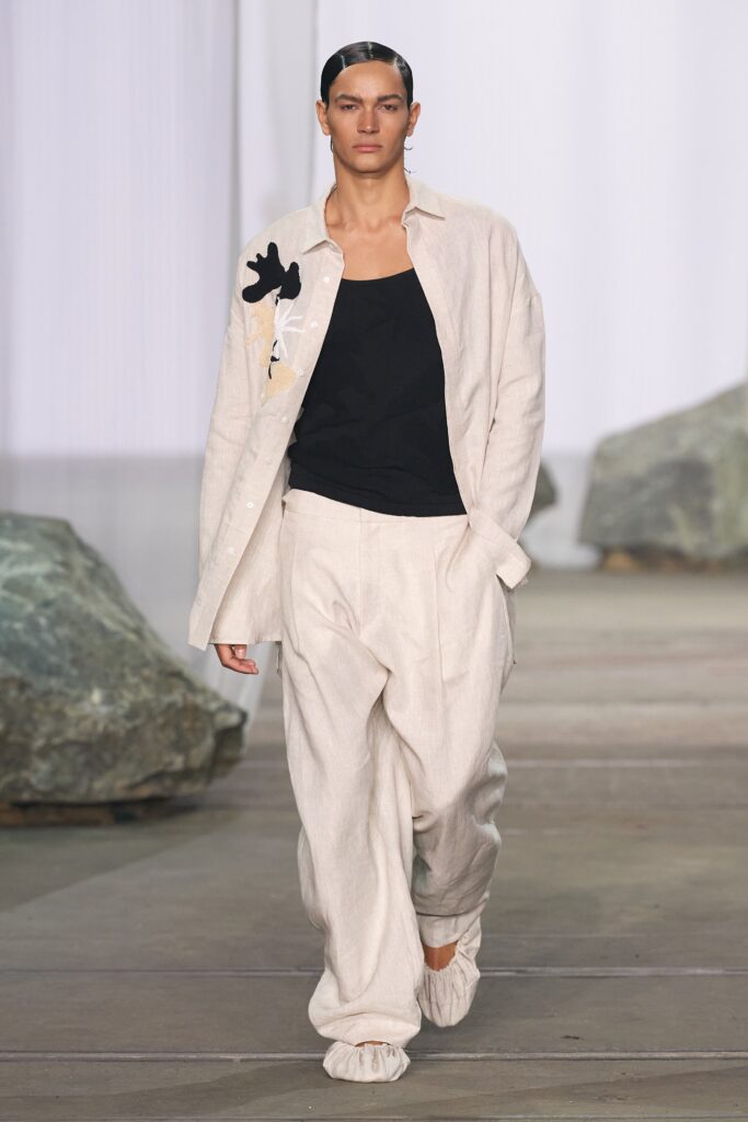 A relaxed-fit beige cotton shirt with a collared design paired with black pants.