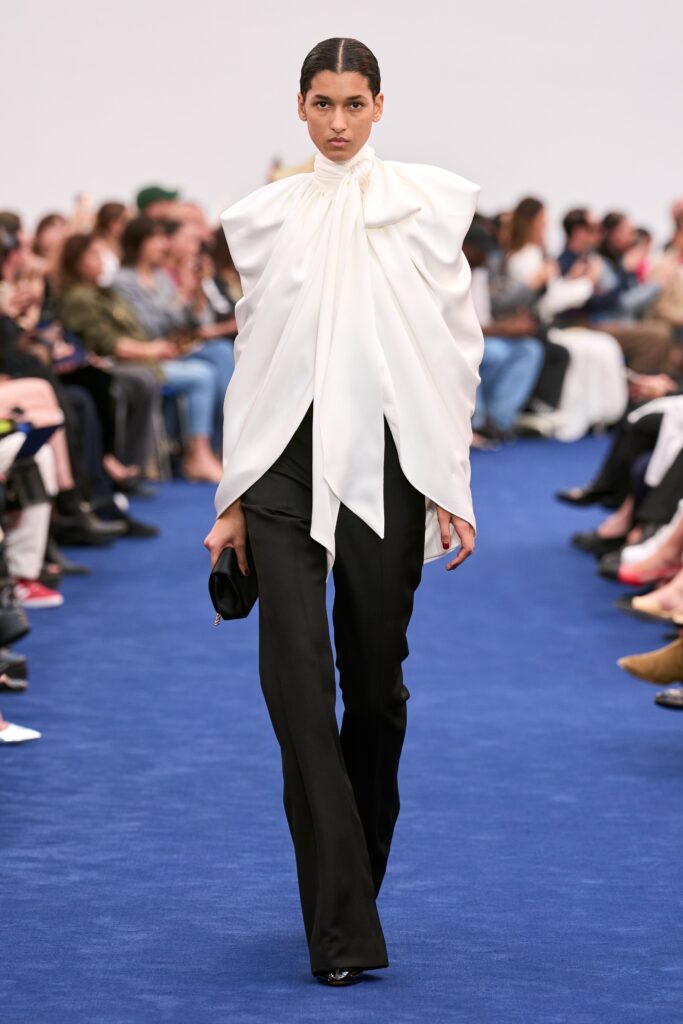 A fitted ensemble featuring black pants and a white layered top with a high neckline.