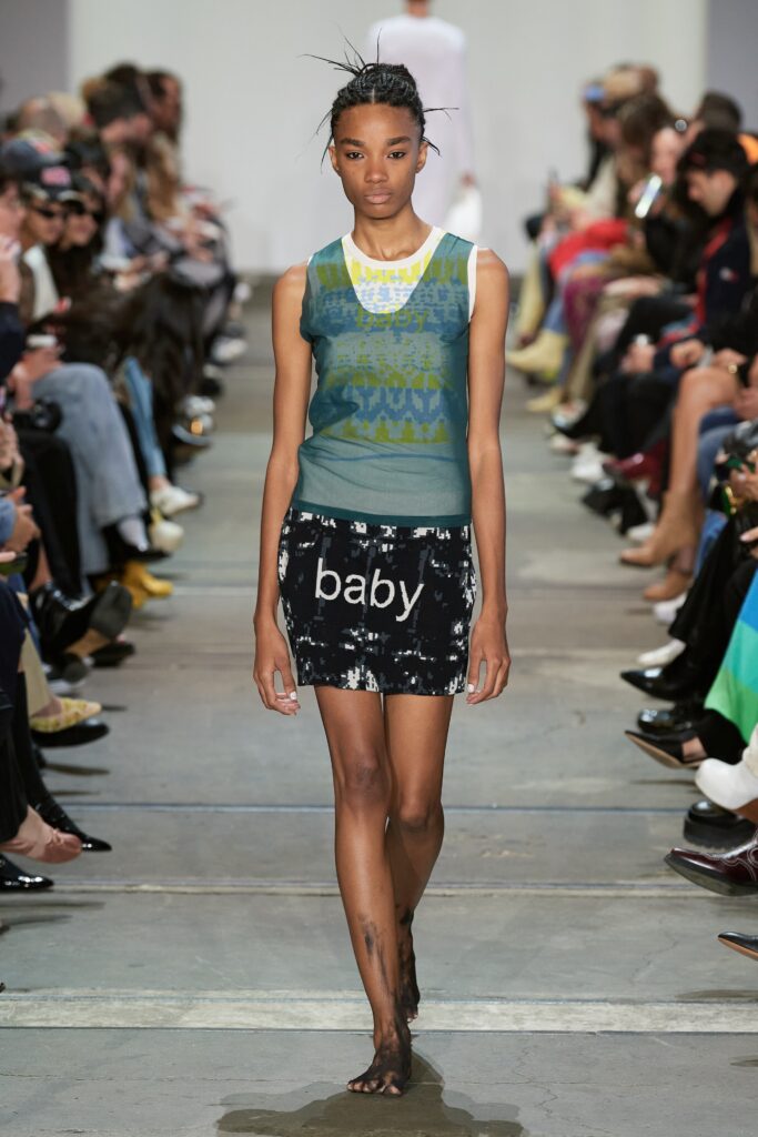 A fitted green sleeveless top with a high-neck and a black mini skirt featuring a printed design.