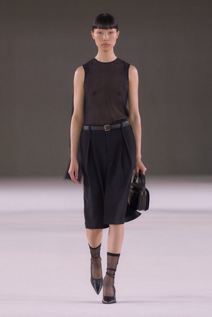 A relaxed black sleeveless top with a high-neck paired with a pleated black skirt.