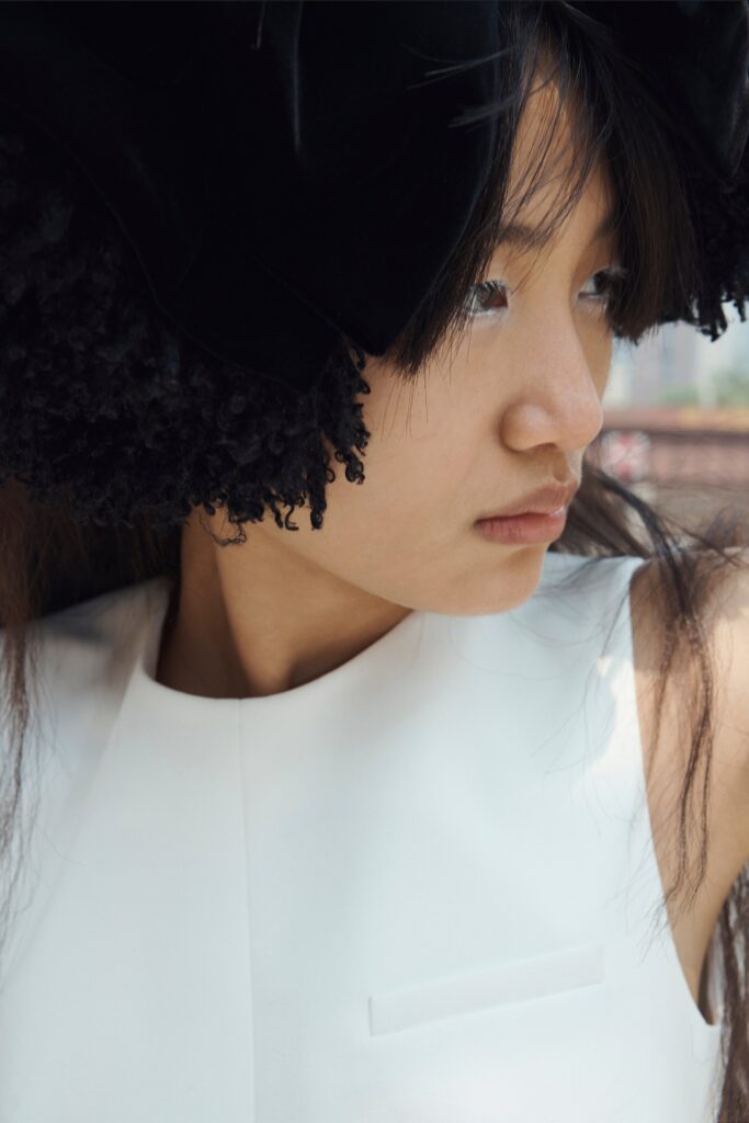 A fitted white silk top with a sleeveless design and high-neck construction.