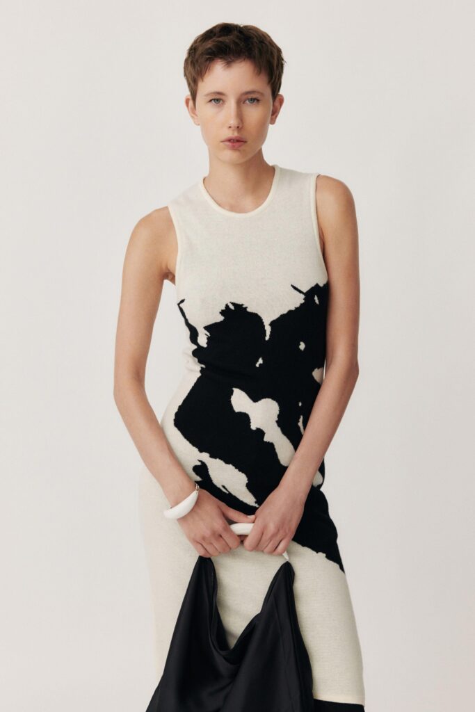 A fitted black and white sleeveless dress with a high neckline and asymmetric design.