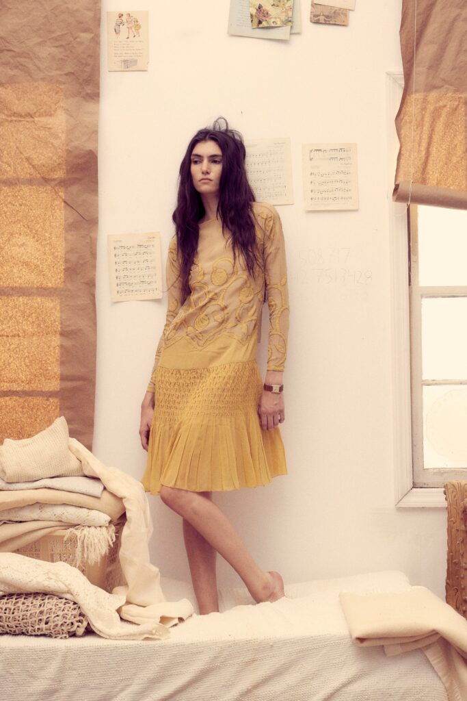 A fitted yellow cotton dress with long sleeves, high neckline, and tiered embroidered details.