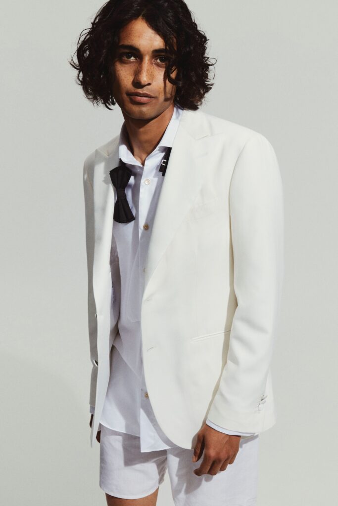 A fitted white blazer paired with a collared long-sleeve shirt, featuring button details.