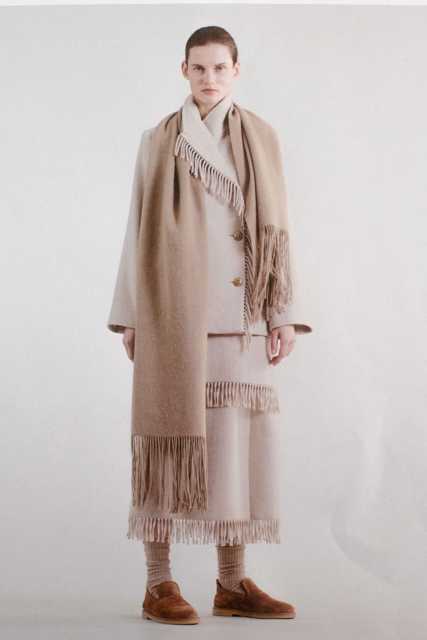 A relaxed beige wool coat with a collared neckline and fringed layered skirt.
