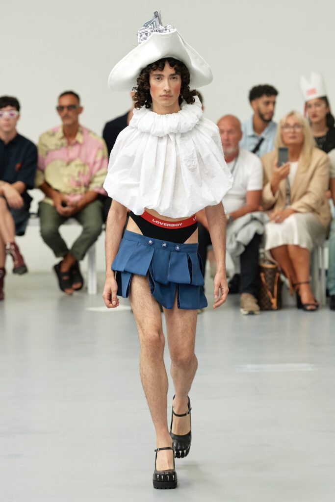 A fitted white cotton sleeveless top with a collared design and an asymmetric blue pleated skirt.