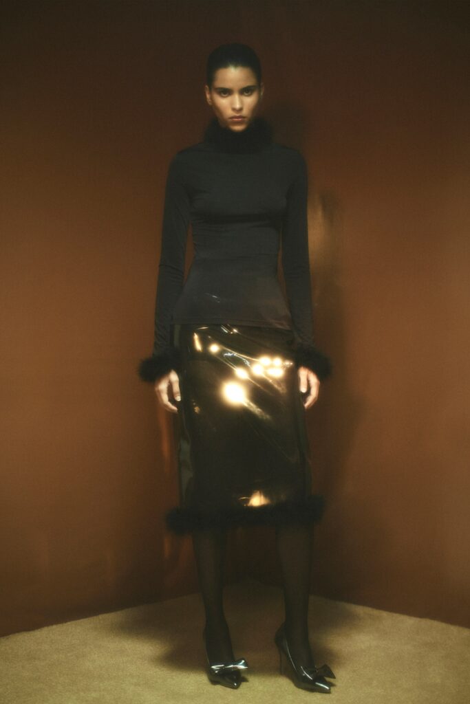A fitted black silk long-sleeve top with a turtleneck paired with a metallic gold skirt featuring an asymmetric slit.