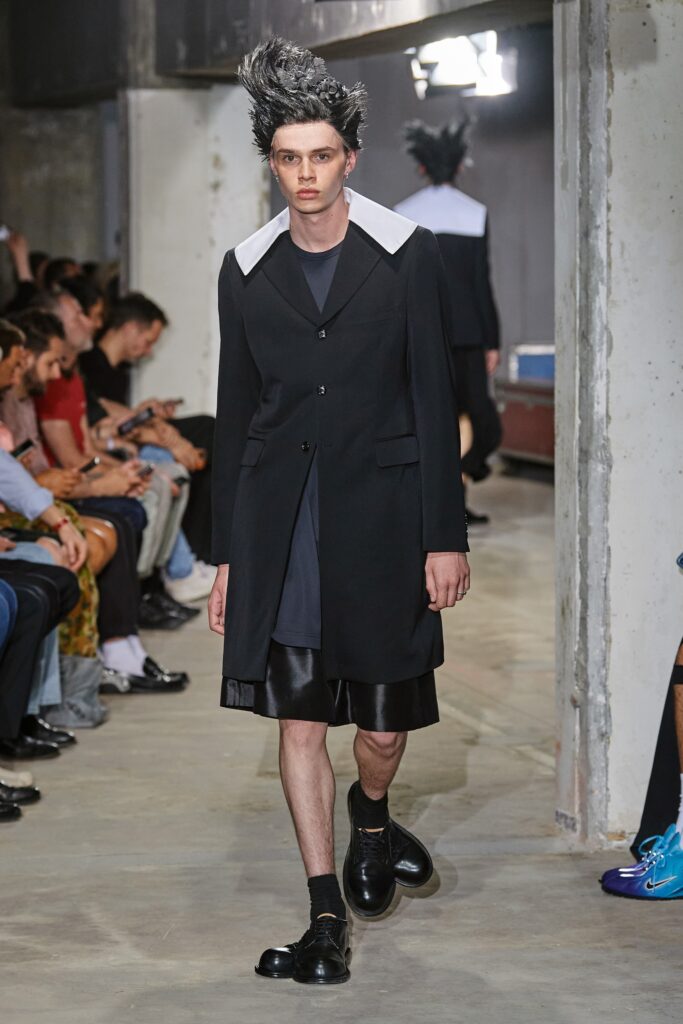 A relaxed black coat dress with a collared neckline and asymmetric design details.