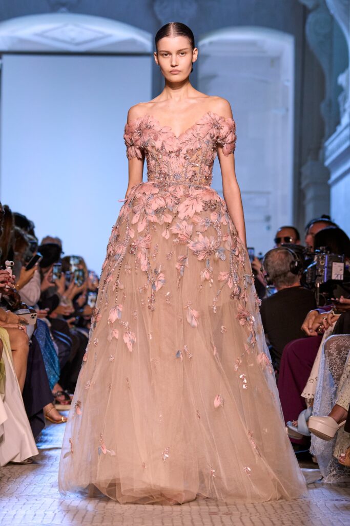 A fitted off-shoulder gown in beige and pink with embroidered details and a tiered silhouette.