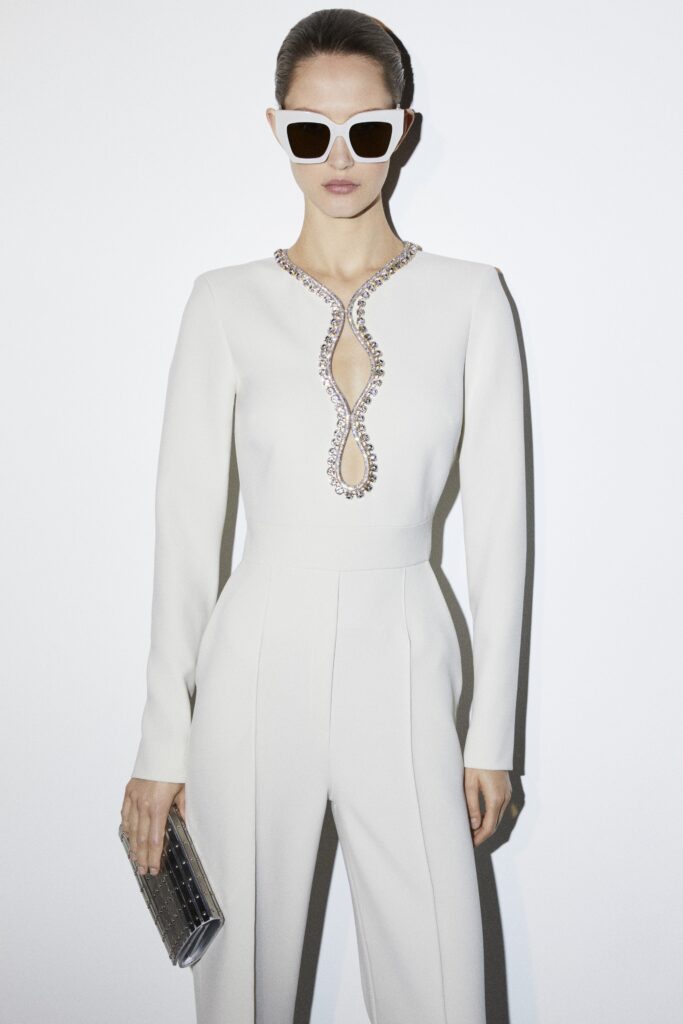 A fitted white neoprene jumpsuit with long sleeves and a V-neckline featuring a zippered detail.