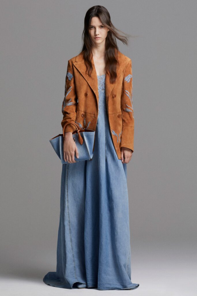 A fitted blue denim maxi dress paired with a brown embroidered leather jacket.
