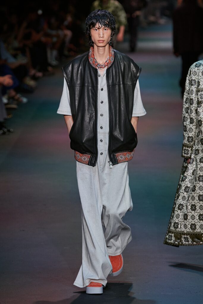 A relaxed black leather sleeveless vest paired with collared gray pants featuring a wide-leg design.