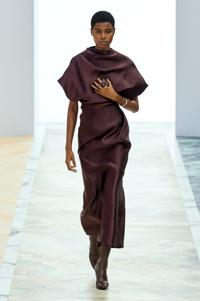 A fitted burgundy silk dress with short sleeves and a high neckline, featuring a draped design.