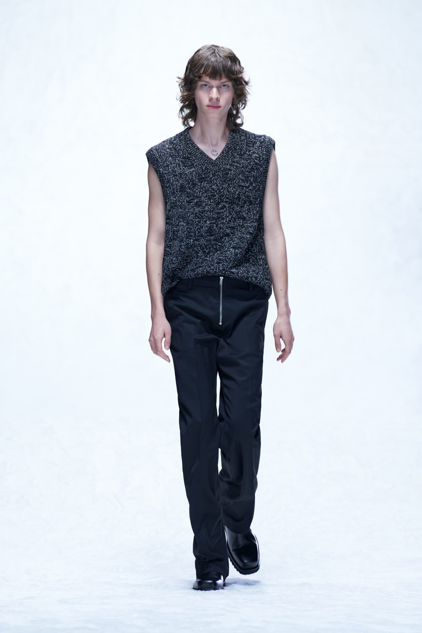 A fitted gray sleeveless top with a V-neckline paired with sleek black pants featuring a zippered detail.