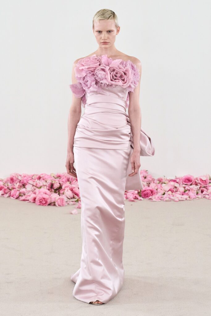 A fitted pink silk gown with an off-shoulder design and ruffled floral details.