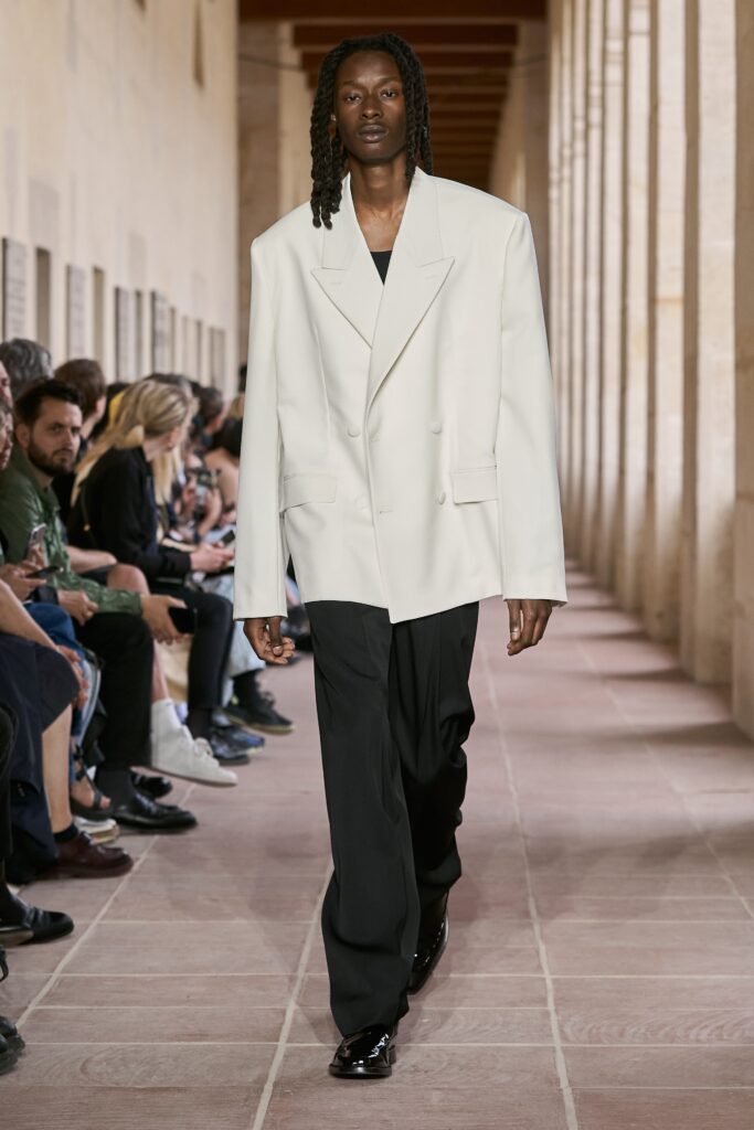 An oversized white jacket with long sleeves and collared design paired with straight-leg black pants.