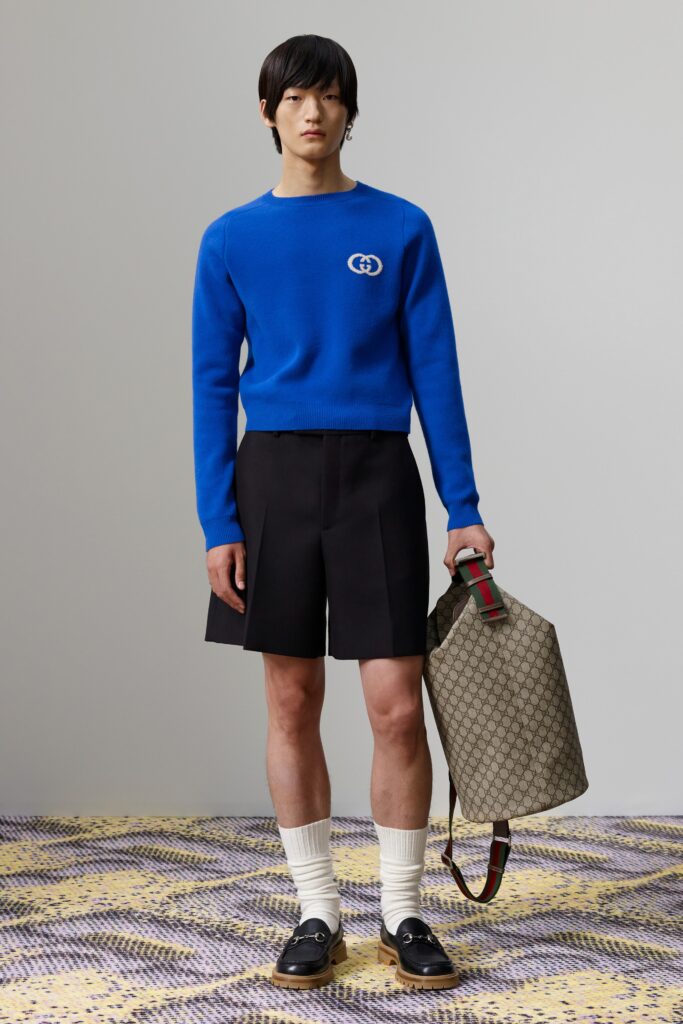 A fitted blue cotton sweater with long sleeves paired with pleated black shorts.