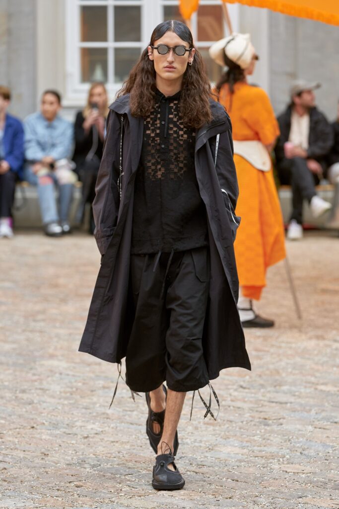 A relaxed black coat with long sleeves and high-waisted pants, featuring a layered design.