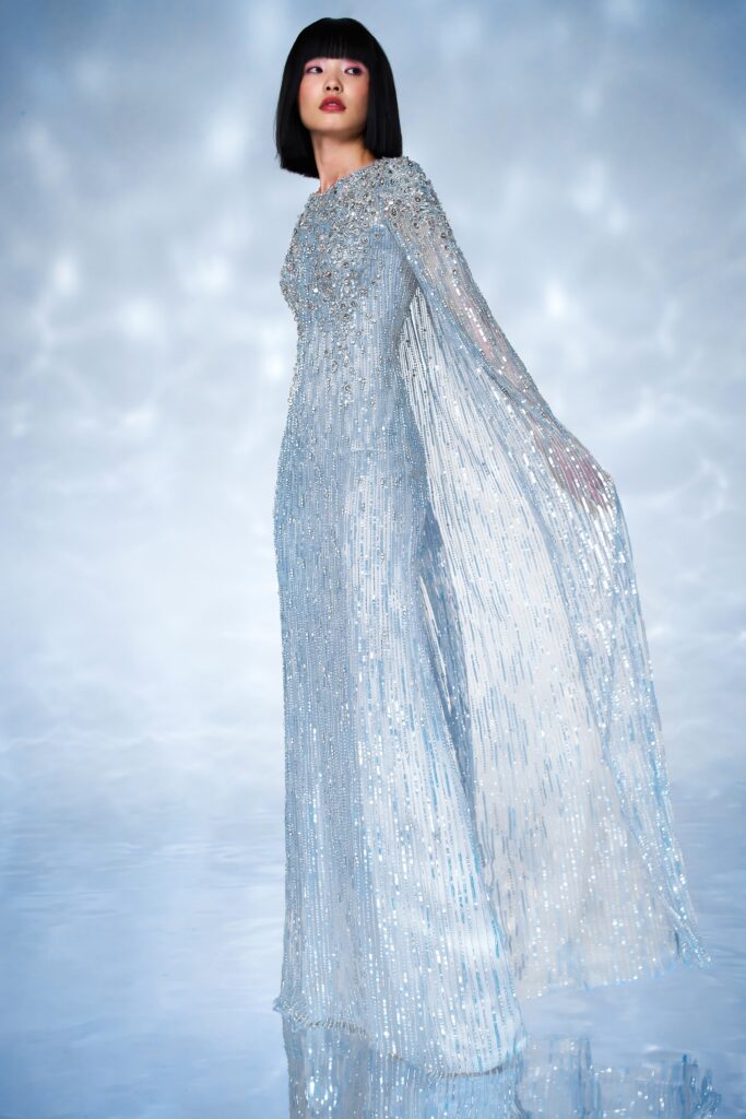 A fitted blue silk gown with long sleeves, high neckline, and draped sequined detailing.