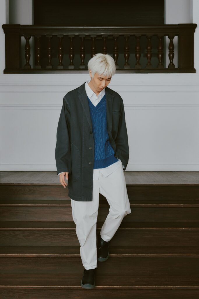 A relaxed fit blue sweater layered under a black jacket with a collared neckline.