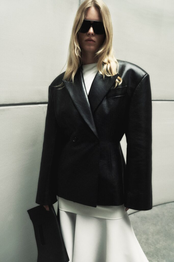 An oversized black leather jacket layered over a white dress with an asymmetric silhouette.
