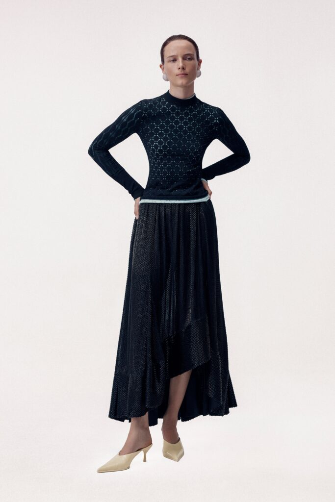A fitted black silk dress with long sleeves, a high neckline, and an asymmetric silhouette.