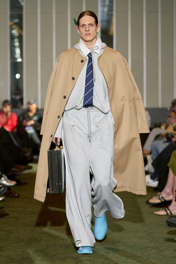 A relaxed-fit beige coat paired with gray pants, featuring a collared neckline and zippered details.