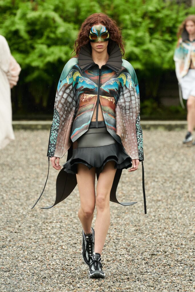 A fitted black dress with a multicolor cape, featuring an asymmetric layered design and sleeveless construction.