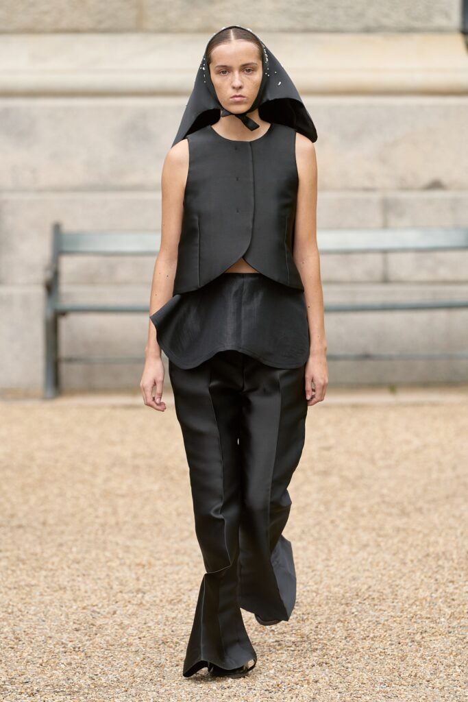 A fitted black silk sleeveless top with a high-neck and asymmetric design paired with matching pants.