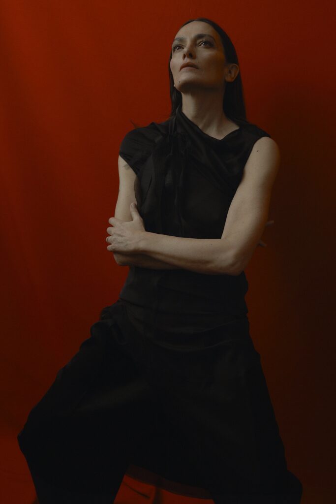 A relaxed black silk sleeveless dress with an asymmetric design and high neckline.