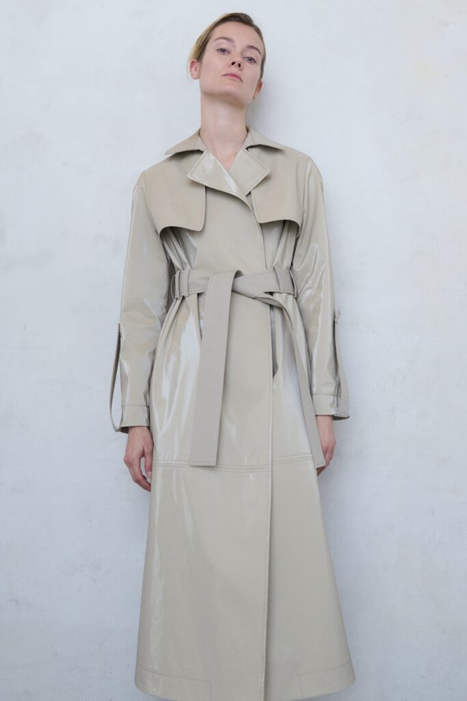 A fitted beige leather trench coat with long sleeves and a belted design.