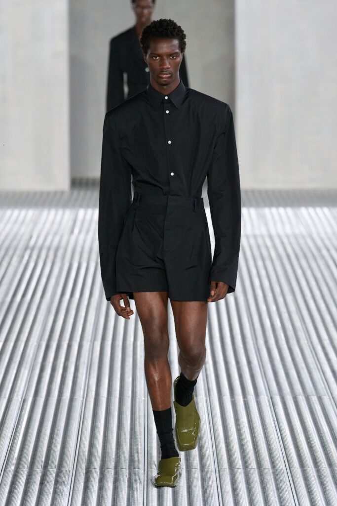 A fitted black shirt with long sleeves and collared design paired with tailored shorts.